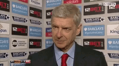 a man in a suit and tie is standing in front of a wall with advertisements for barclays and sky sports