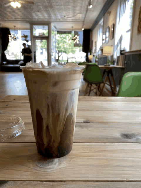 a cup of iced coffee sits on a wooden table in a restaurant