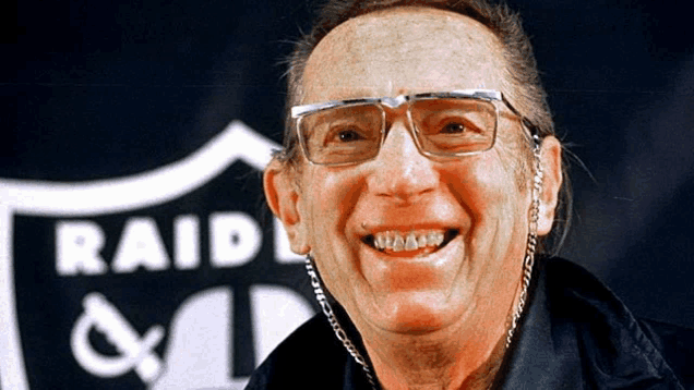 a man is smiling in front of a raiders sign