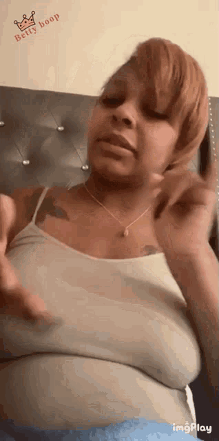 a woman in a white tank top is sitting in front of a bed and making a funny face .