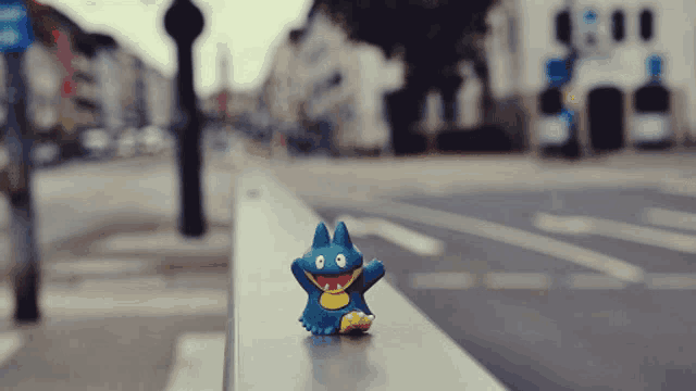 a blue toy with yellow teeth is sitting on a railing in front of a street