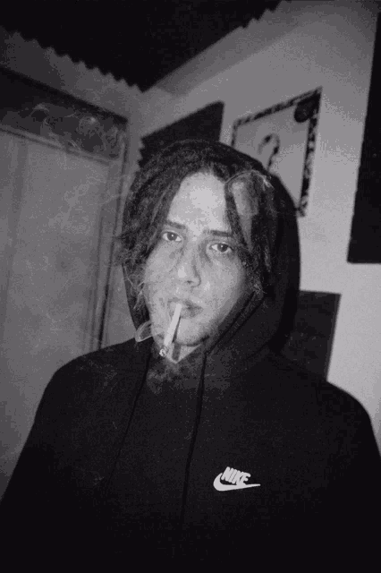 a man with dreadlocks wearing a black nike hoodie smoking a cigarette