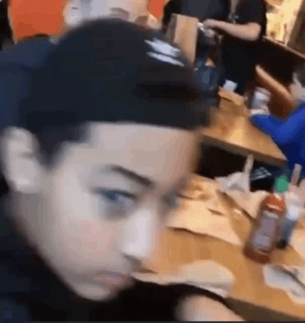 a young boy is sitting at a table in a restaurant with a bottle of ketchup on the table .