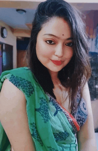 a woman in a green saree and a blue top is smiling .