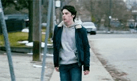 a young man is walking down a sidewalk wearing a blue jacket and a hoodie .