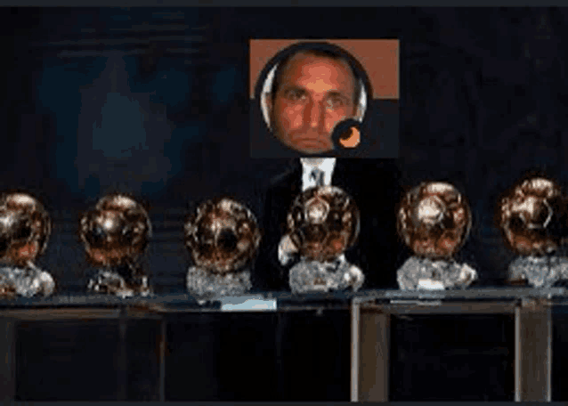 a man in a suit is standing in front of a row of soccer trophies .