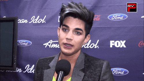 a man speaking into a microphone in front of a wall that says american idol and fox