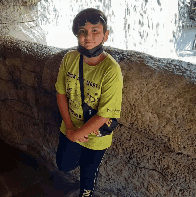 a boy wearing a green rick and morty shirt stands in front of a waterfall