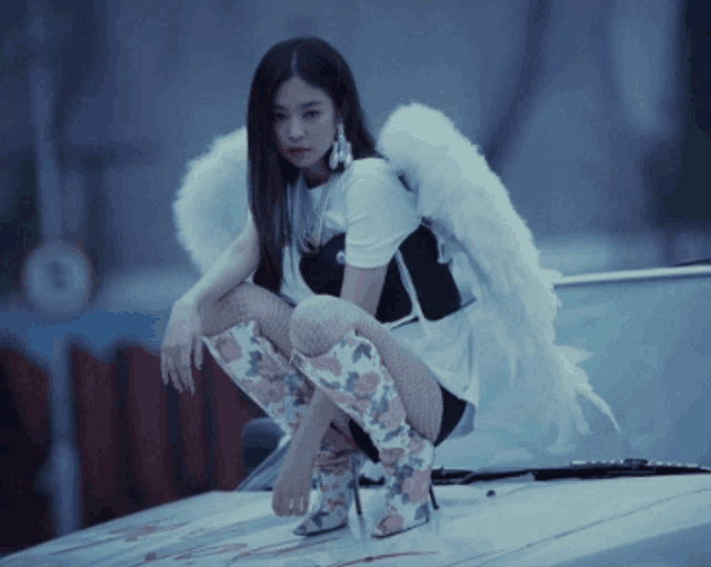 a woman wearing angel wings and knee high boots sits on the hood of a car