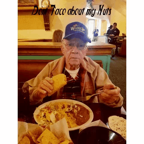 an elderly man is sitting at a table with a plate of food and a sign that says don 't taco