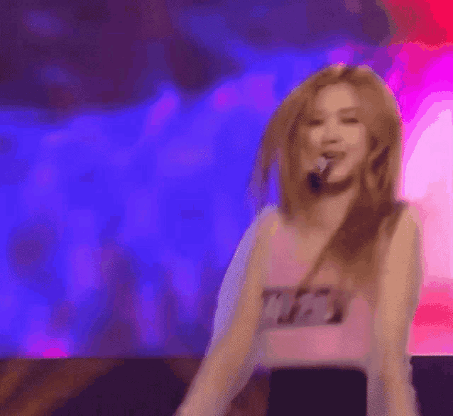 a woman is singing into a microphone on a stage in front of a colorful background .