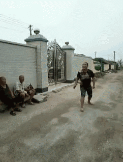 a group of people are sitting on a bench on the side of a dirt road while a man is running down the road .