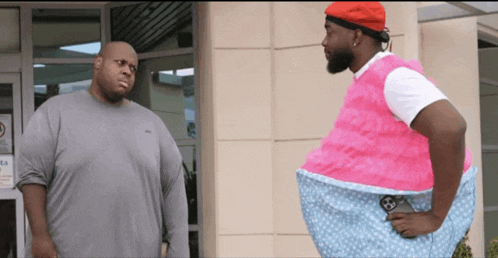 two men are standing in front of a building and one of them is wearing a pink outfit