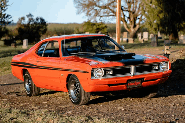 a red and black dodge car is parked in a graveyard