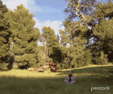 a woman sits in a lotus position in a field with peacock written on the bottom right