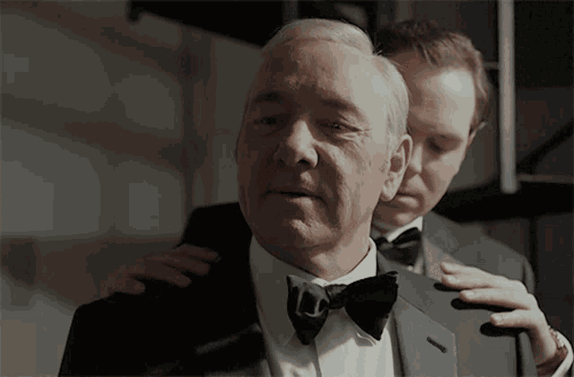 a man in a tuxedo and bow tie is being hugged by another man