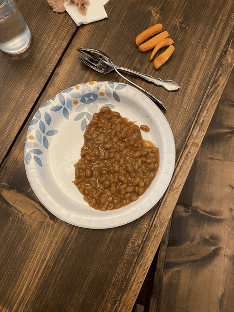 a paper plate filled with baked beans and carrots