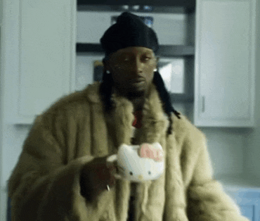 a man in a fur coat is holding a hello kitty mug in his hand .