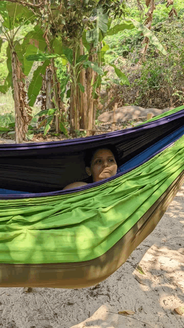 a woman is laying in a green hammock on a beach