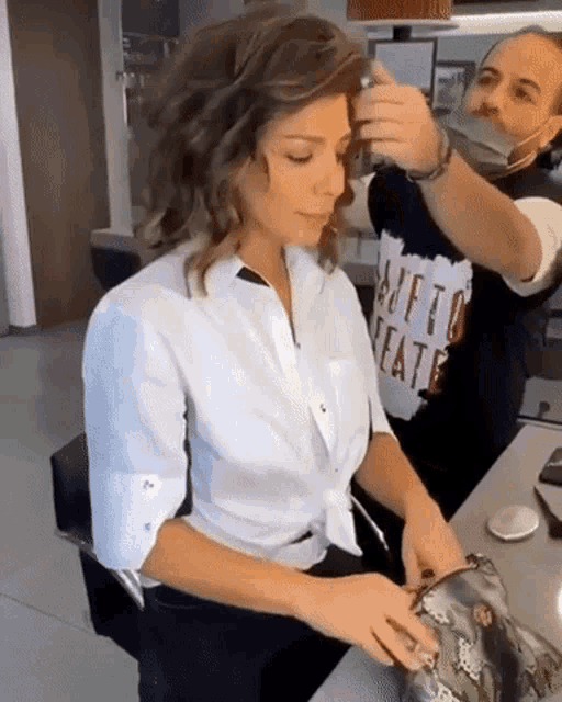 a woman in a white shirt is getting her hair done by a man wearing a black shirt that says " tutto teatro "