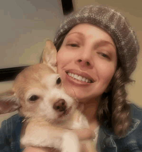 a woman in a hat is holding a small dog and smiling