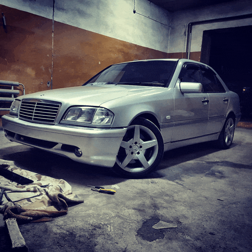 a silver mercedes is parked in a garage with a yellow screwdriver on the ground