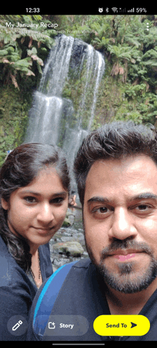 a man and a woman are posing for a picture in front of a waterfall and the time is 12:33