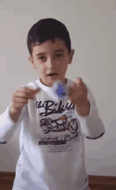 a young boy wearing a white shirt with the word bikes on it is holding a blue object in his hands .