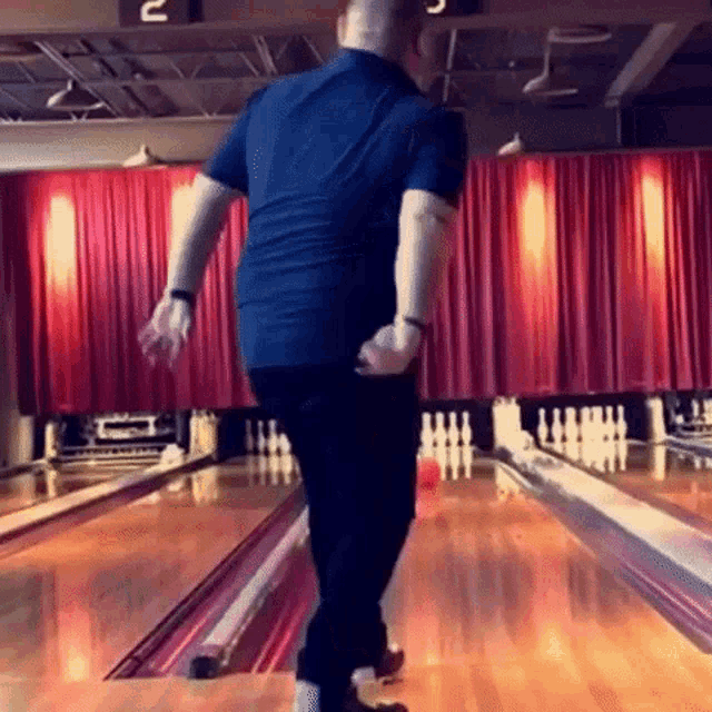 a man in a blue shirt is bowling on a bowling alley with the number 2 on the wall behind him