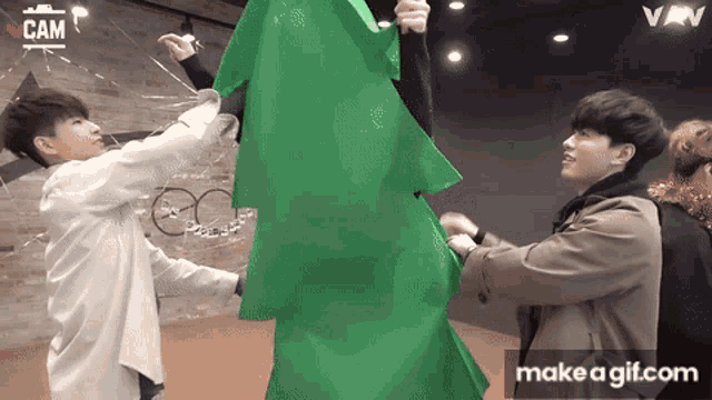 a group of young men standing around a green christmas tree .