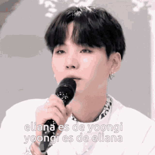 a young man is singing into a microphone with the words eliana es de yoongi yoongi es de eliana .