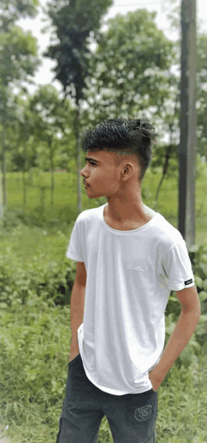 a young man wearing a white t-shirt and black shorts is standing in a field with his hands in his pockets