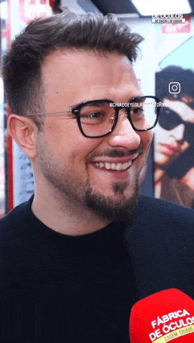 a man wearing glasses is smiling in front of a red microphone that says fabrica de culos on it