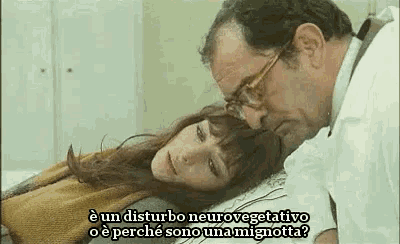 a man is talking to a woman who is laying on a bed with a blanket on her head .