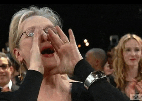 a woman wearing glasses is covering her face with her hands in a crowd .