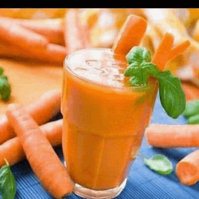 a glass of carrot juice is surrounded by carrots and basil leaves .