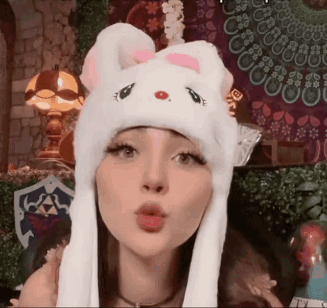 a woman wearing a white bunny hat is blowing a kiss