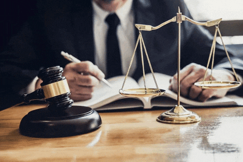 a man sitting at a table with a book and a scale of justice