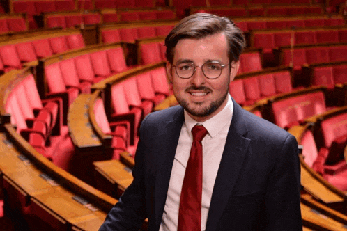 a man in a suit and tie stands in front of a row of red chairs