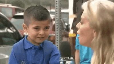 a young boy in a blue shirt is talking to a woman with a microphone in front of him .