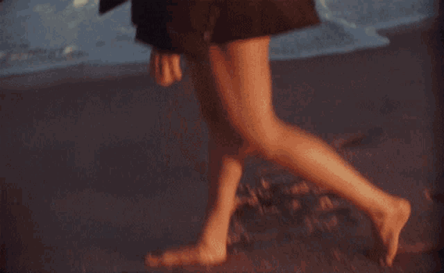 a woman in a black coat is standing on a beach near the ocean