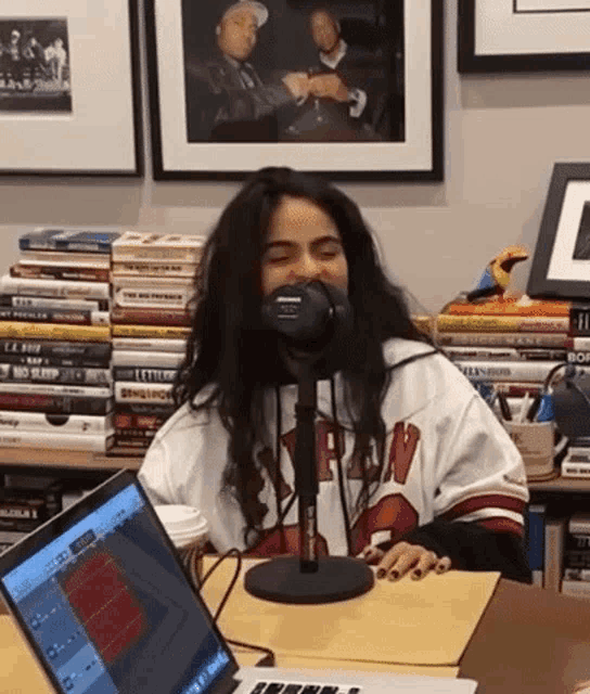 a woman is sitting at a desk in front of a microphone and a laptop .