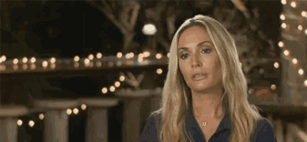 a woman in a blue shirt is standing in front of a string of lights and making a funny face .