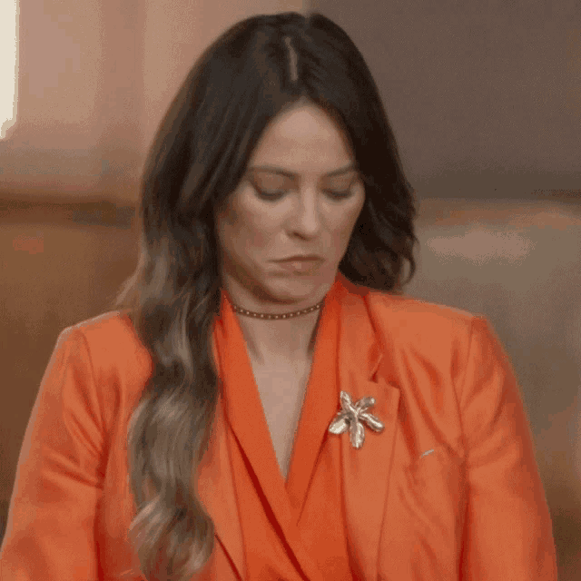 a woman wearing an orange jacket has a brooch on her chest