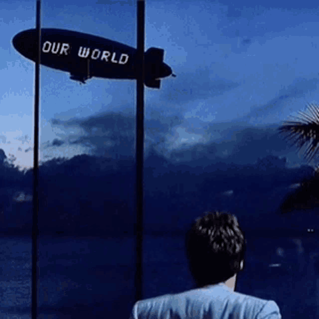 a man stands in front of a zeppelin that says our world