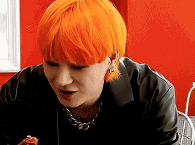 a woman with orange hair is sitting at a table with a plate of food .