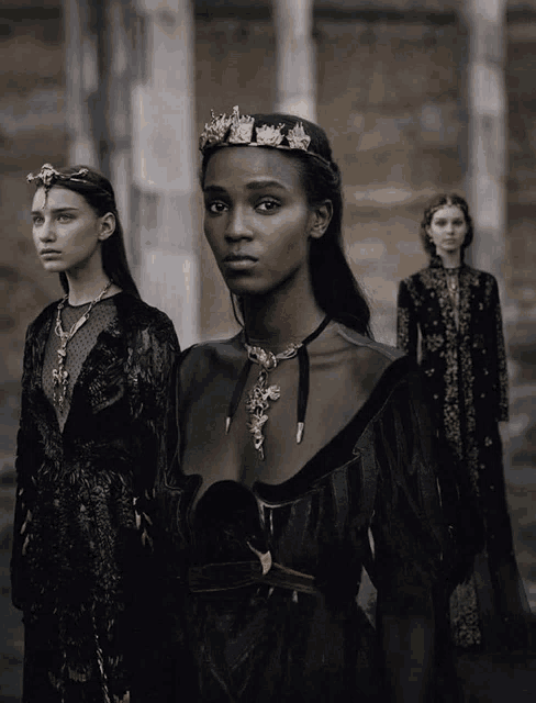 a woman with a crown on her head is standing next to two other women in black dresses