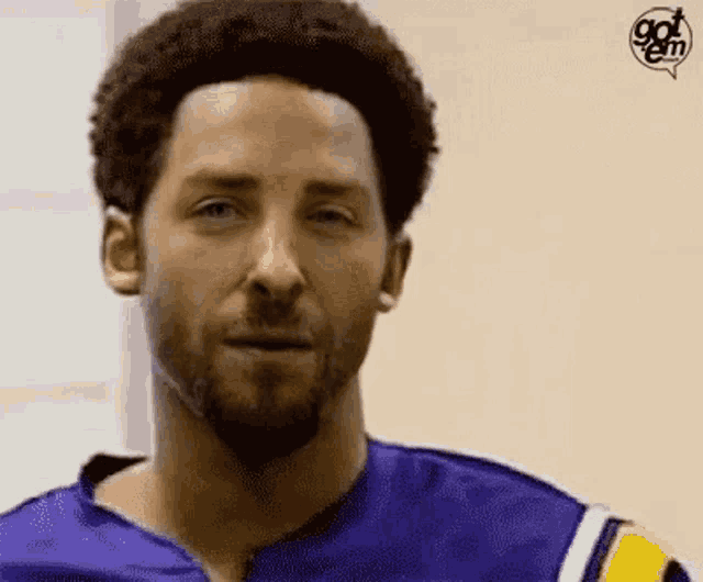 a man with a beard wearing a blue and yellow jersey is making a funny face .