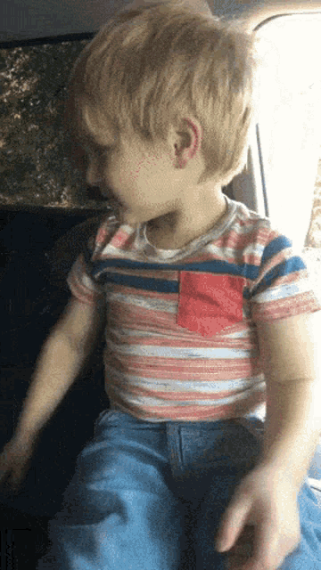 a young boy wearing a red white and blue striped shirt is sitting in a car