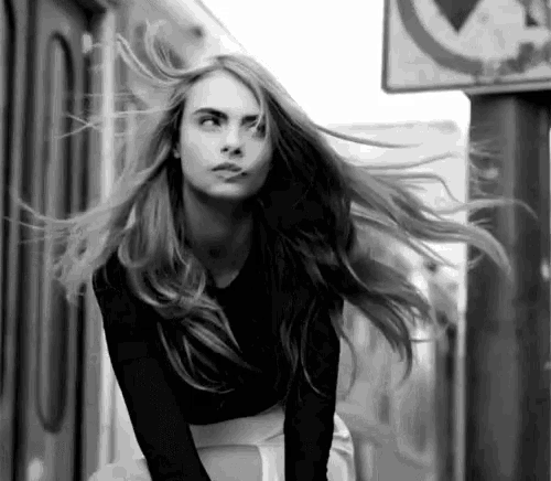 a black and white photo of a woman with long hair standing in front of a no parking sign .